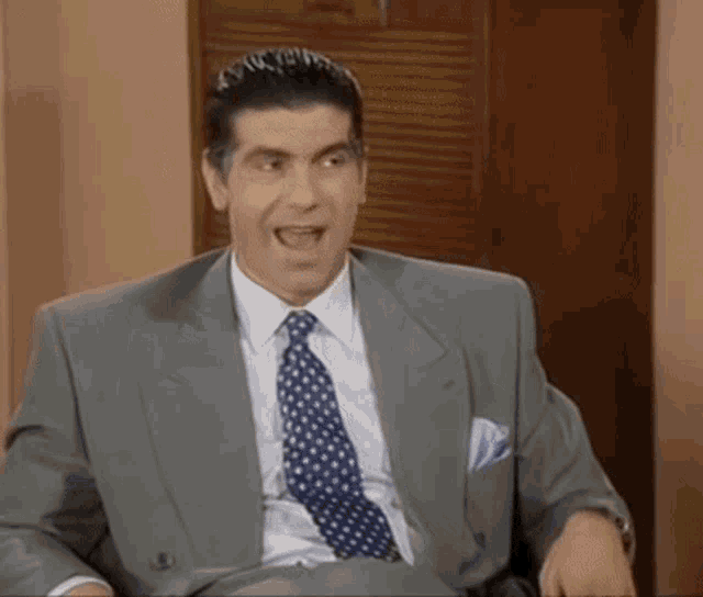 a man in a suit and tie is sitting in a chair and smiling .