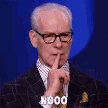 a man in a suit and tie is holding his finger to his mouth and says nooo .
