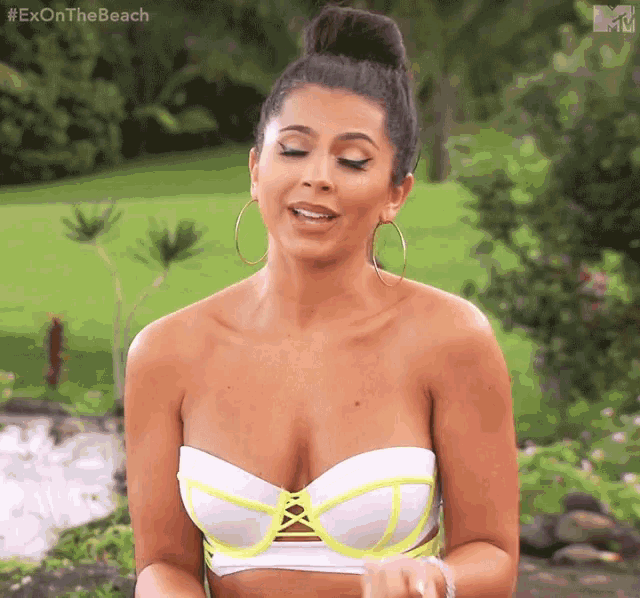 a woman in a white and yellow bikini top is standing in a garden .