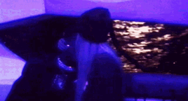 a person is singing into a microphone in a dark room with purple lights .