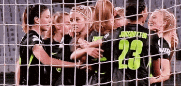 a group of female soccer players are hugging behind a net and one of them has the number 23 on her jersey