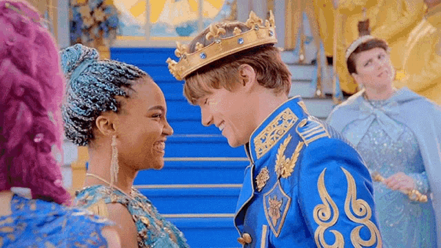 a man in a crown is standing next to a woman in a blue dress and looking at her .