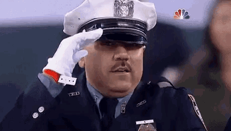 a police officer wearing a hat and gloves salutes at a game .