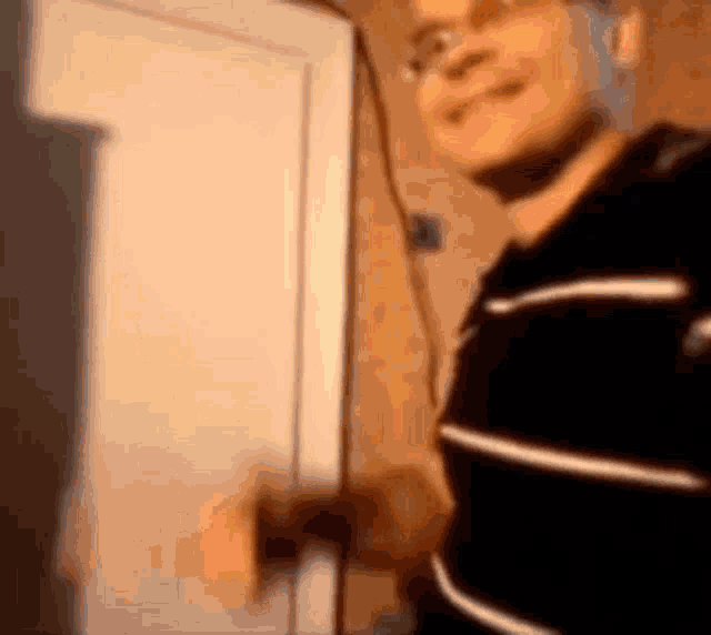 a man in a black and white striped shirt is standing in front of a door and smiling .