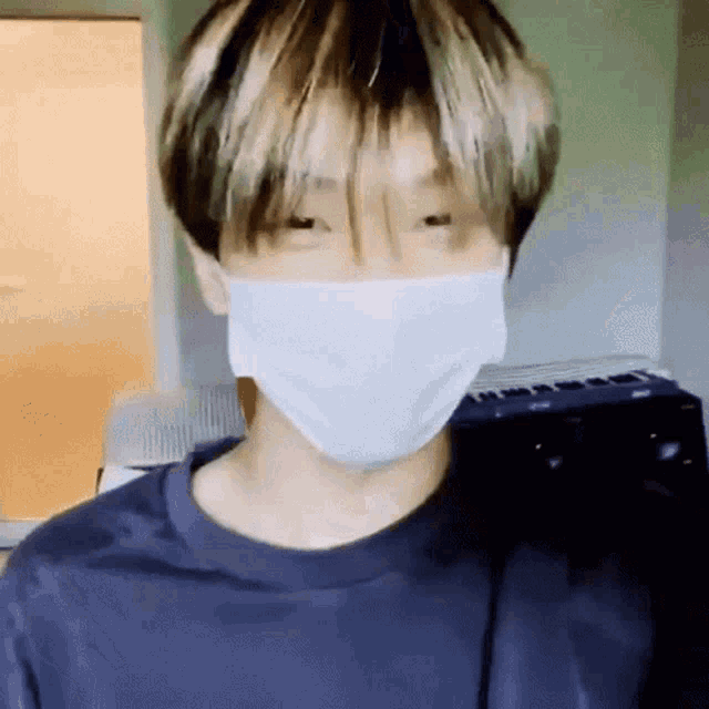 a young man wearing a face mask and a blue shirt is standing in a room .