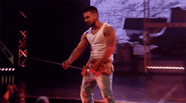 a man in a white tank top is standing on a stage holding a rope