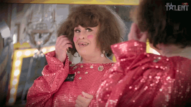 a woman in a pink sequined dress is looking at herself in a mirror with the word talent on the bottom