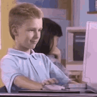 a young boy is sitting in front of a computer and smiling .