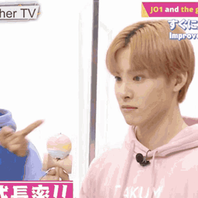 a young man in a pink hoodie is holding a toy and pointing at another person .