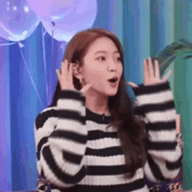a woman wearing a striped sweater is sitting in front of balloons .