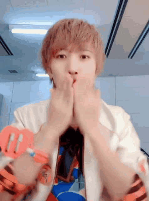 a young man covering his mouth with his hands while wearing a white shirt