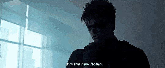 a man in a robin costume is standing in front of a window and saying i 'm the new robin .