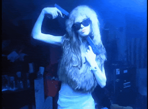 a woman wearing sunglasses and a fur vest holds a gun