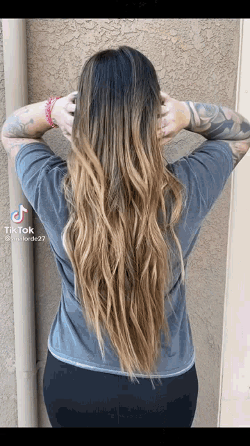 a woman with long hair is holding her hair in front of a wall .