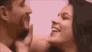 a man and a woman are kissing each other and smiling . the woman is touching the man 's face .