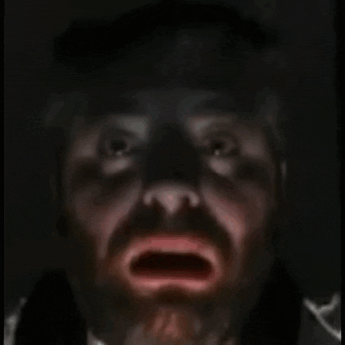 a man with a beard is screaming in the dark with his mouth open .