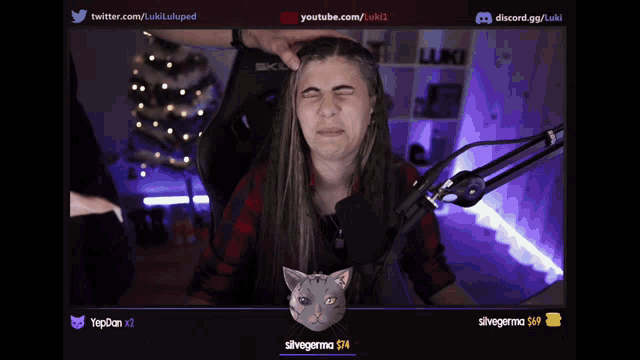 a woman is making a funny face in front of a microphone with a cat behind her