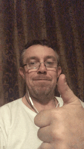 a man wearing glasses and a white shirt gives a thumbs up
