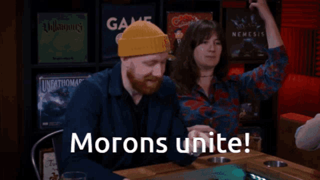 a man and a woman are sitting at a table with the words morons unite on the screen