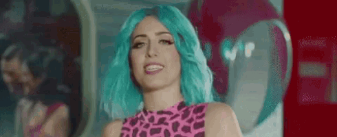 a woman with blue hair and a pink leopard print top is smiling in front of a mirror .
