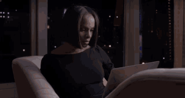 a woman in a black dress is sitting on a couch using an apple laptop
