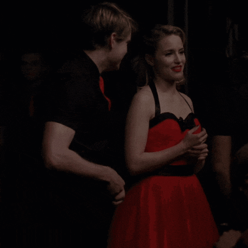a woman in a red dress stands next to a man in a black shirt and red tie