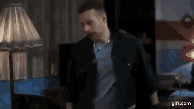 a man with a mustache is standing in a living room with a lamp .