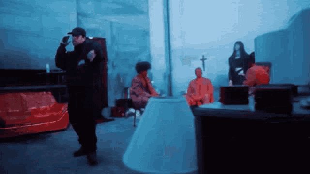 a man in a black jacket stands in a dark room with a cross on the wall