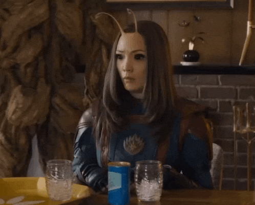 a woman in a superhero costume is sitting at a table with glasses and a can of soda .