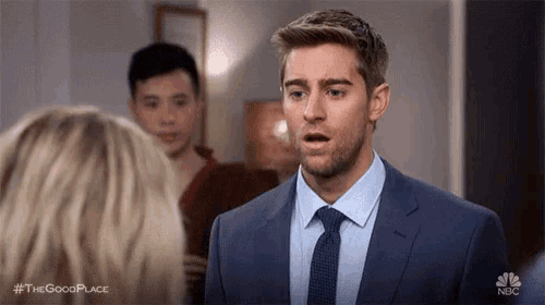a man in a suit and tie is talking to a woman and making a surprised face .