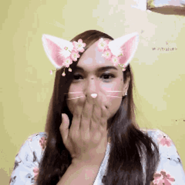 a woman wearing cat ears and flowers on her face covering her mouth