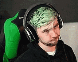 a man with green hair is wearing headphones while sitting in a chair .