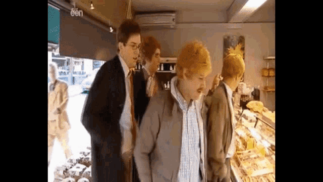 a group of men are standing in front of a bakery . one of the men has red hair .