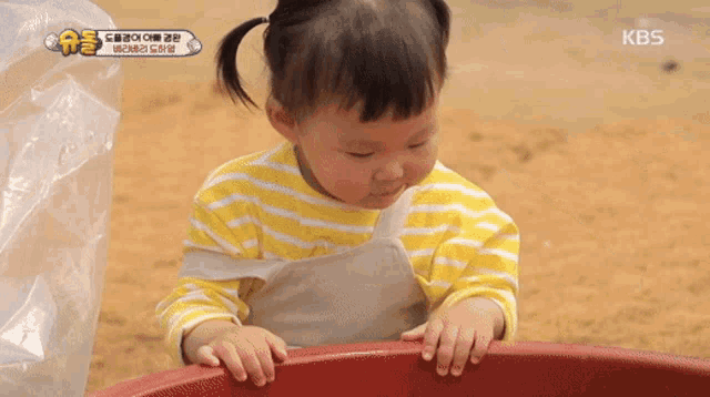 a little girl in a yellow and white striped shirt is playing with a red container .
