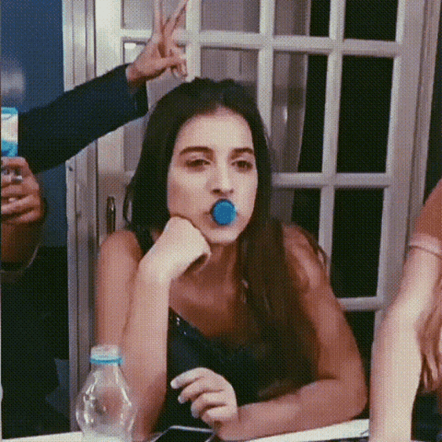 a woman with a blue lollipop in her mouth is sitting at a table