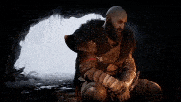 a man with a beard is sitting in a cave holding a sword and looking at his phone .