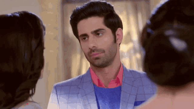 a man in a blue suit and a pink shirt is talking to two women
