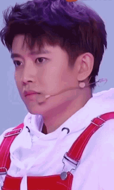 a young man wearing red overalls and a white hoodie with a microphone behind his ear .