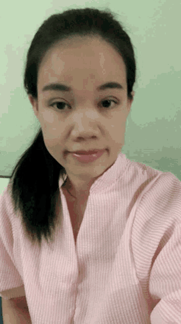 a woman wearing a pink and white striped shirt is taking a selfie