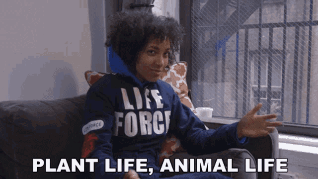 a person wearing a blue life force sweatshirt sits on a couch in front of a window