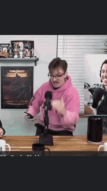 a man in a pink hoodie stands in front of a microphone in a room