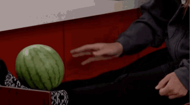 a person 's hand is reaching for a watermelon that is on the floor