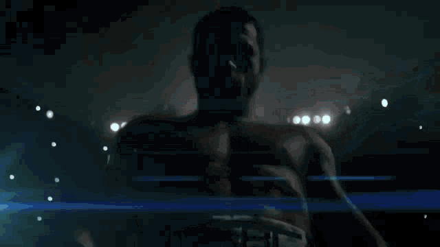 a man without a shirt is in a boxing ring with a blue light behind him