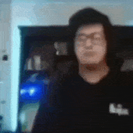 a blurry picture of a man with glasses standing in front of a computer screen .