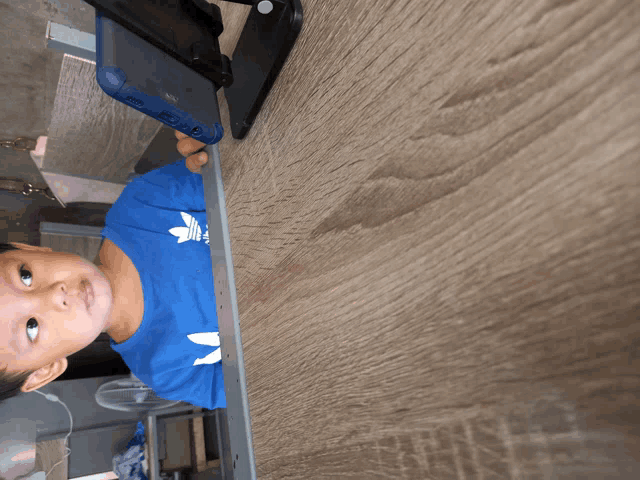 a little boy wearing a blue adidas shirt looks down