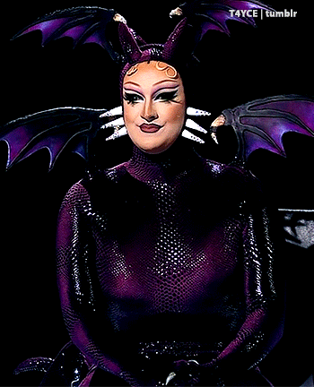 a drag queen in a purple costume with wings and horns is smiling for the camera
