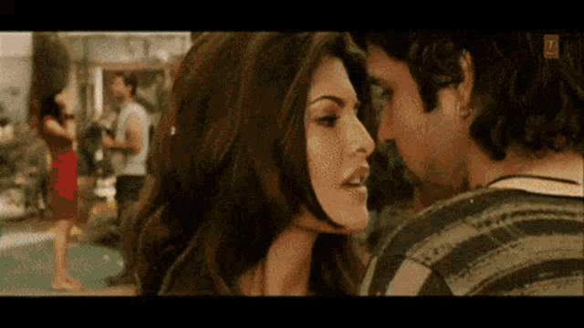 a man and a woman are kissing with a woman in a red dress in the background .