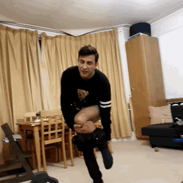 a man in a black sweater with a teddy bear on it is standing in a living room