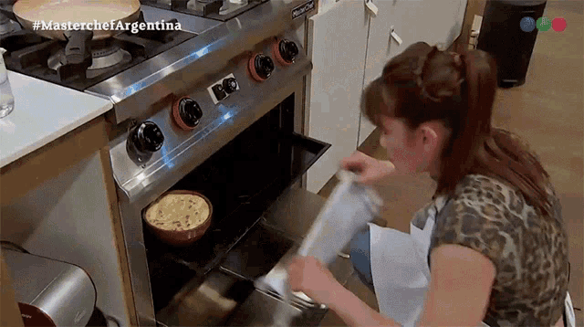 a woman taking a piece of food out of an oven that says masterchef argentina on the bottom