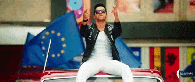 a man is sitting on top of a red car giving the thumbs up sign